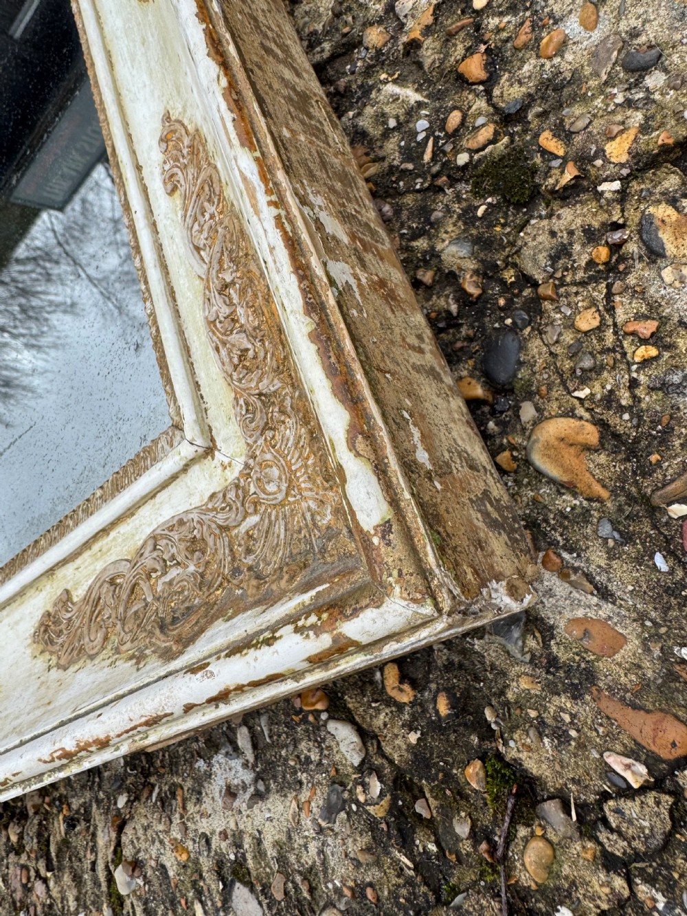 A rectangular antique wall mirror featuring a distressed cream-painted timber frame decorated with gilded corner spandrels and foxed mirror glass. View X