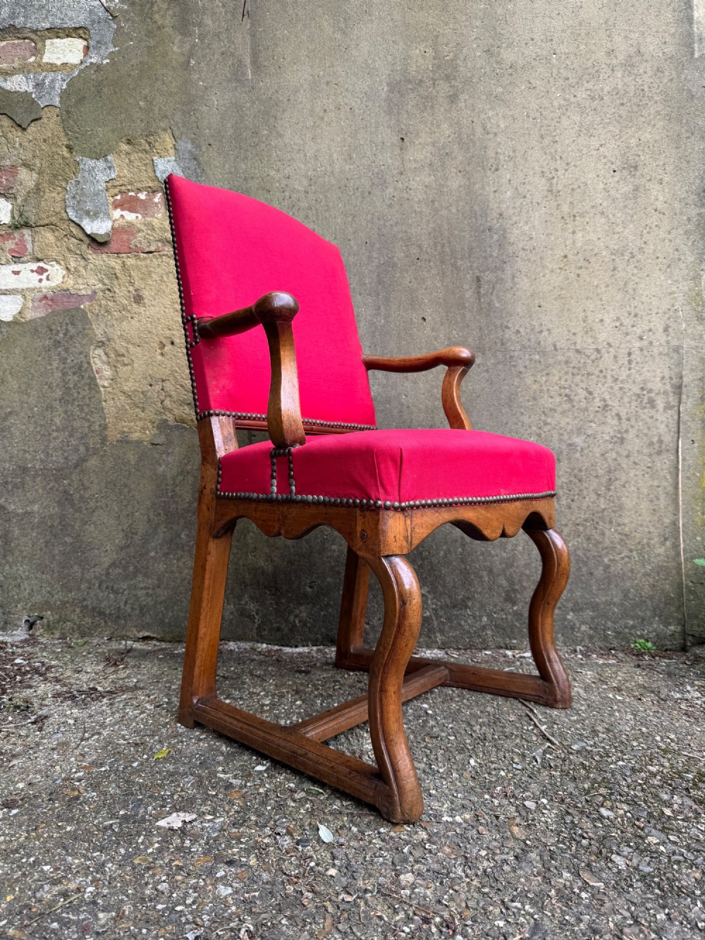 An antique French wooden armchair featuring red fabric upholstery, scrolled arms, brass stud trimming, and a rectangular stretcher base. View II