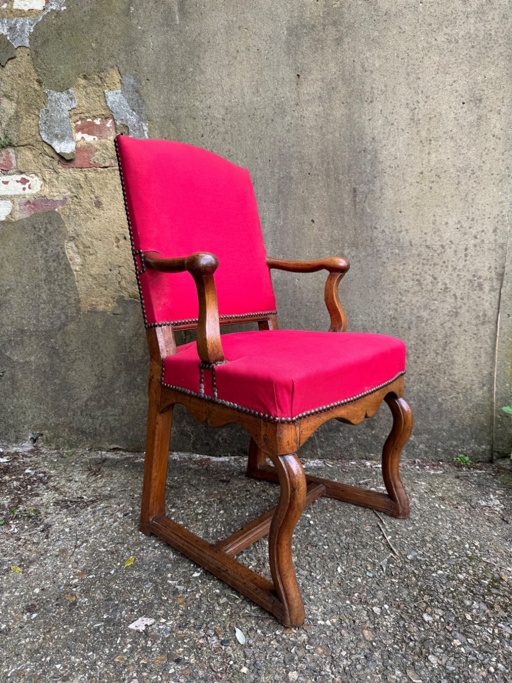 An antique French wooden armchair featuring red fabric upholstery, scrolled arms, brass stud trimming, and a rectangular stretcher base. View III