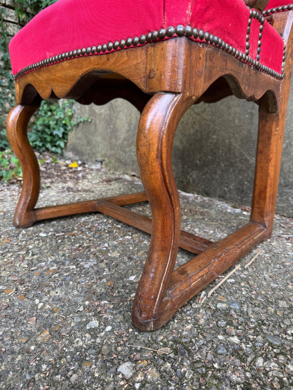 An antique French wooden armchair featuring red fabric upholstery, scrolled arms, brass stud trimming, and a rectangular stretcher base. View VI