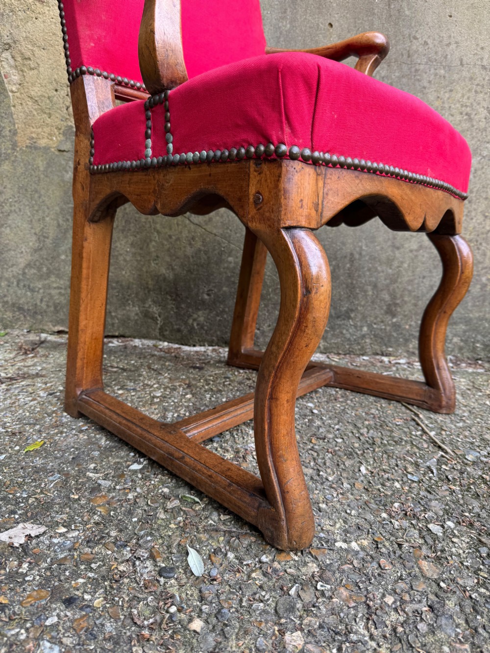 An antique French wooden armchair featuring red fabric upholstery, scrolled arms, brass stud trimming, and a rectangular stretcher base. View IX