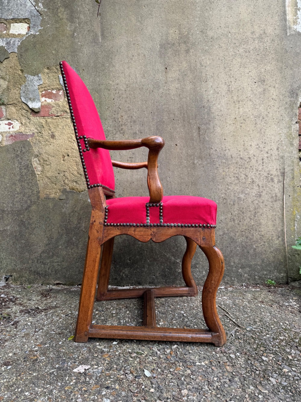 An antique French wooden armchair featuring red fabric upholstery, scrolled arms, brass stud trimming, and a rectangular stretcher base. View X