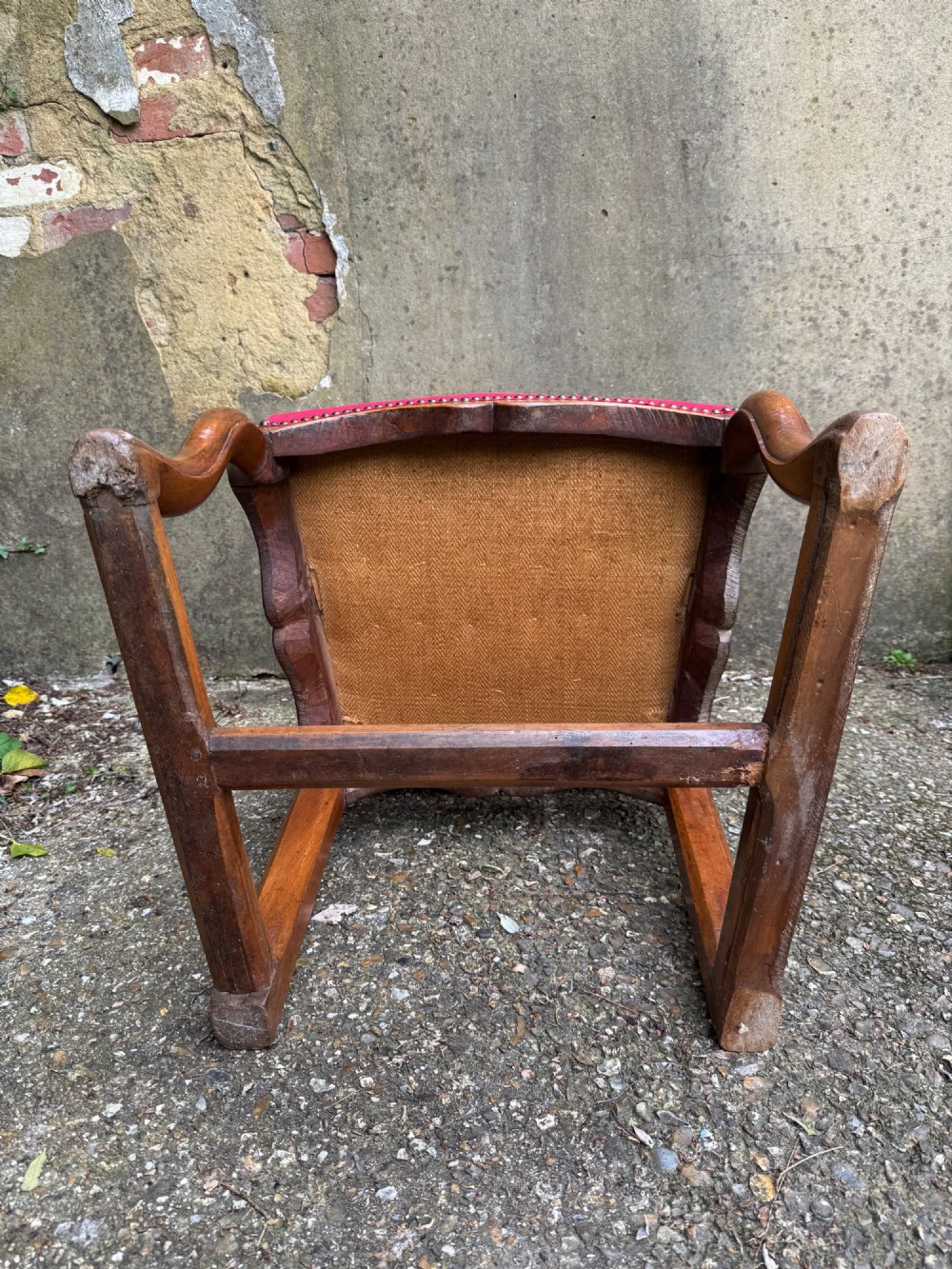 An antique French wooden armchair featuring red fabric upholstery, scrolled arms, brass stud trimming, and a rectangular stretcher base. View XII