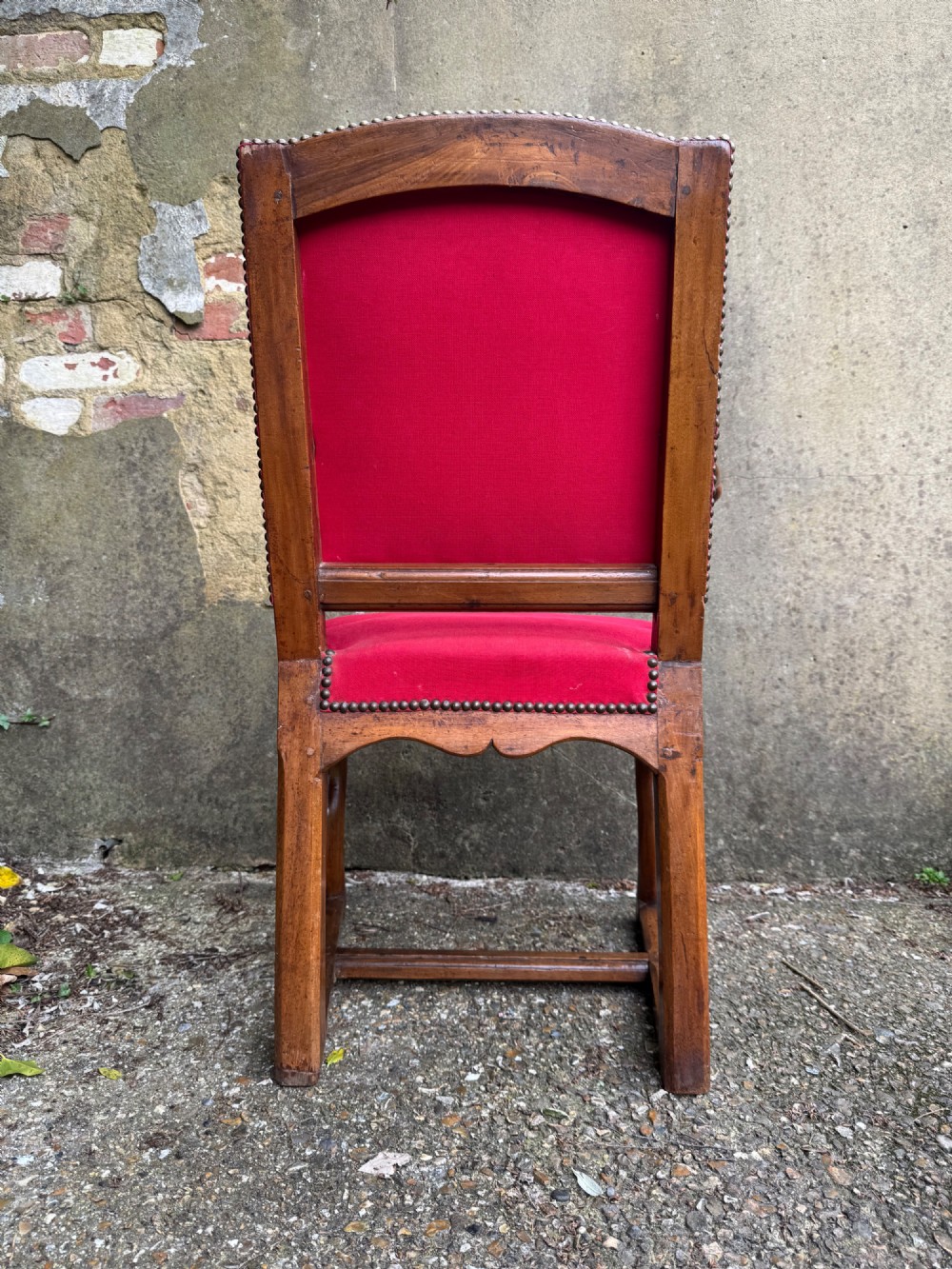 An antique French wooden armchair featuring red fabric upholstery, scrolled arms, brass stud trimming, and a rectangular stretcher base. View XIV