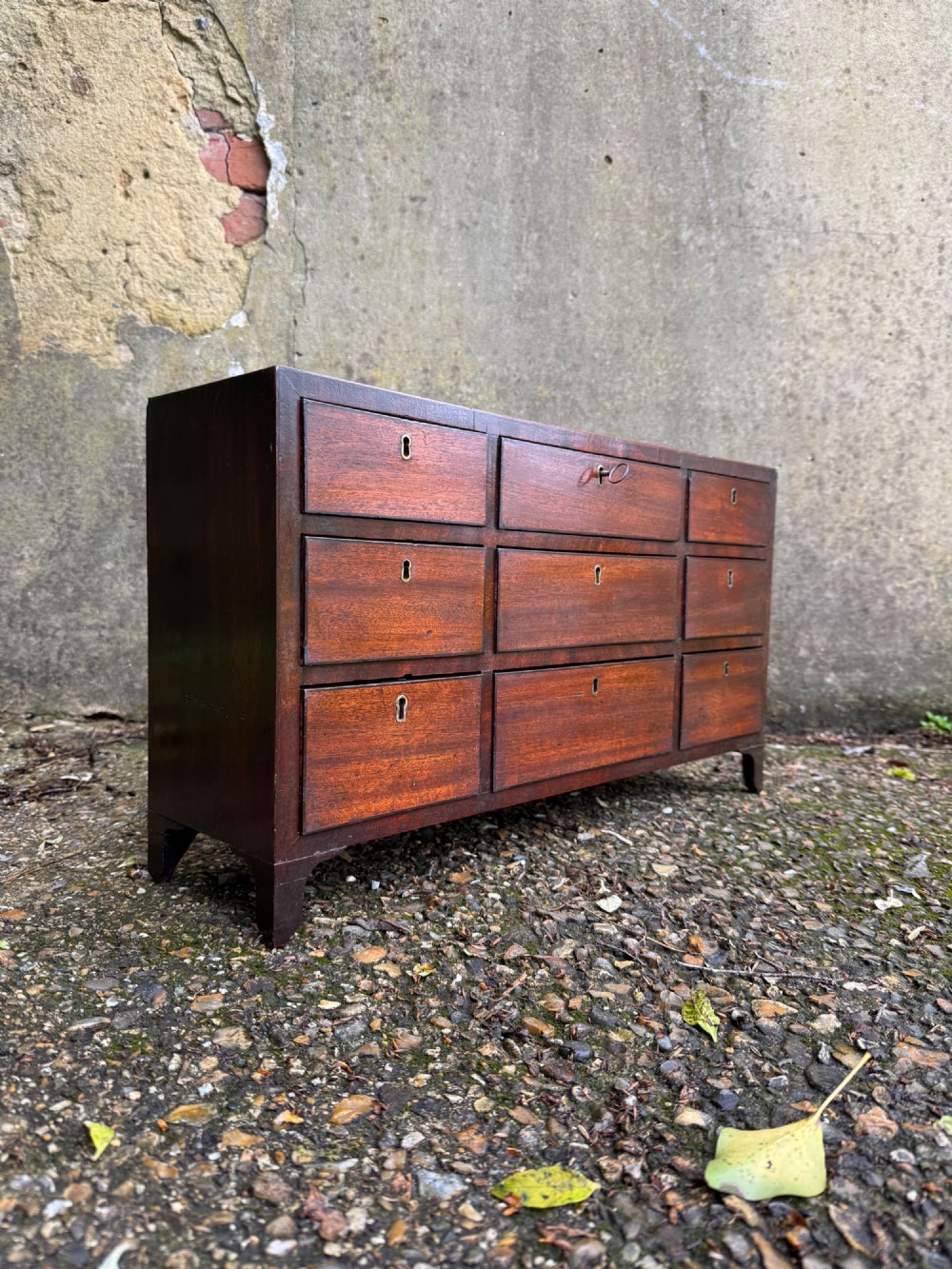 A dark Georgian mahogany flight of nine drawers with brass keyhole escutcheons resting on short bracket feet.