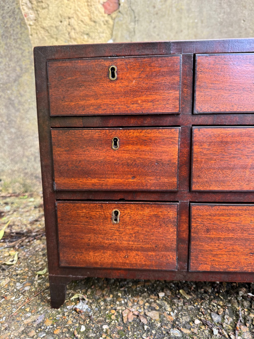 A dark Georgian mahogany flight of nine drawers with brass keyhole escutcheons resting on short bracket feet. View IV