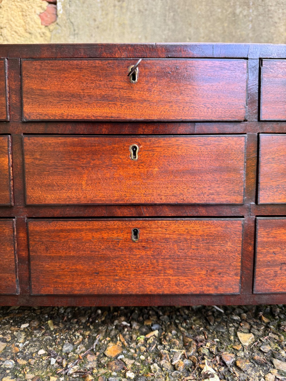 A dark Georgian mahogany flight of nine drawers with brass keyhole escutcheons resting on short bracket feet. View V