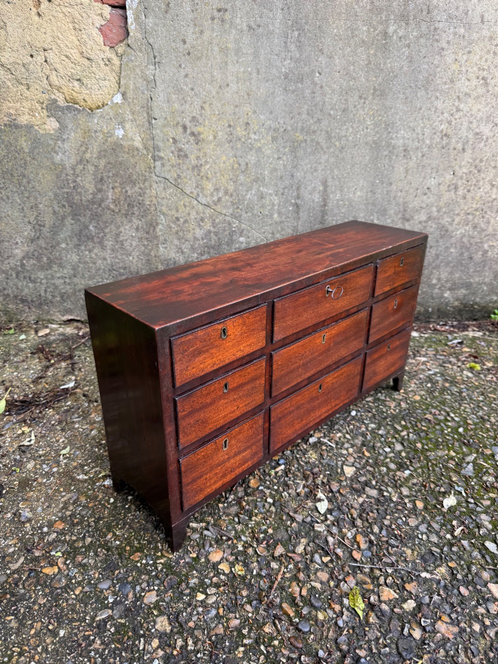 A dark Georgian mahogany flight of nine drawers with brass keyhole escutcheons resting on short bracket feet. View VII