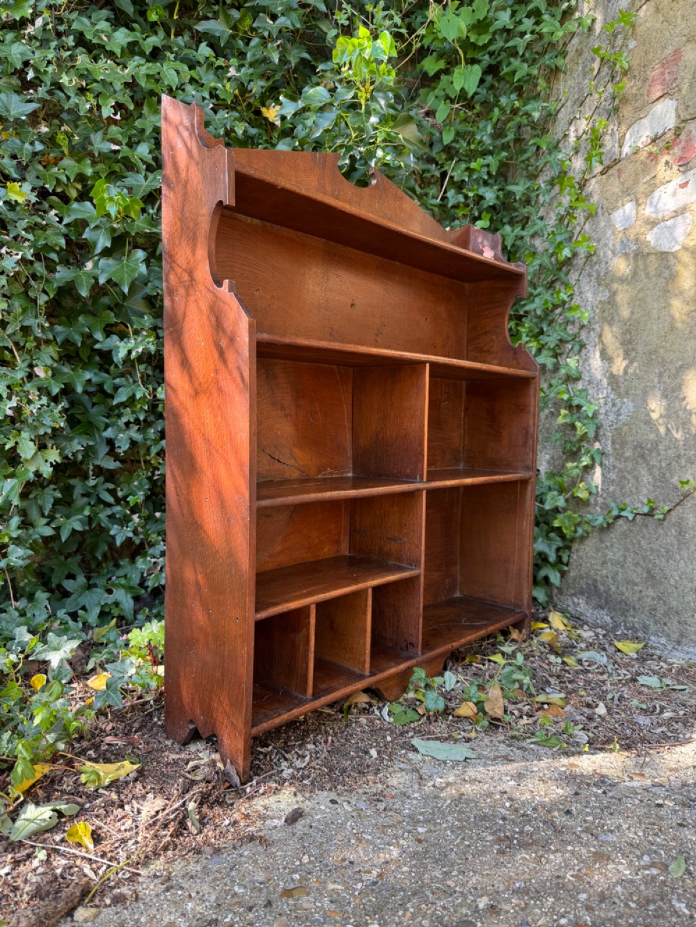 A small antique oak open bookcase featuring multiple shelf compartments, lower cubbies, and shaped side uprights.
