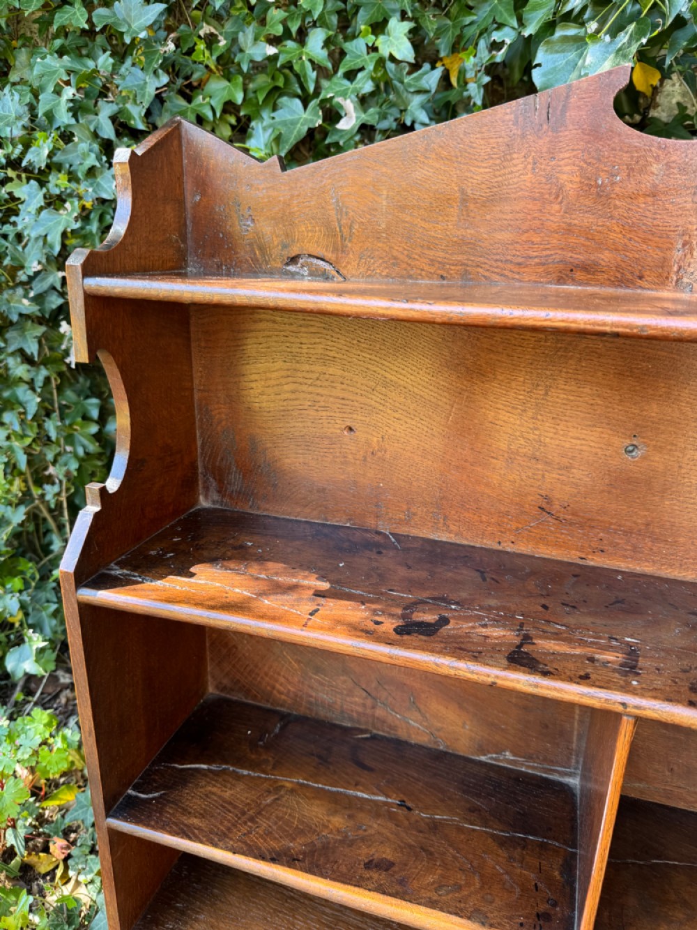 A small antique oak open bookcase featuring multiple shelf compartments, lower cubbies, and shaped side uprights. View VII