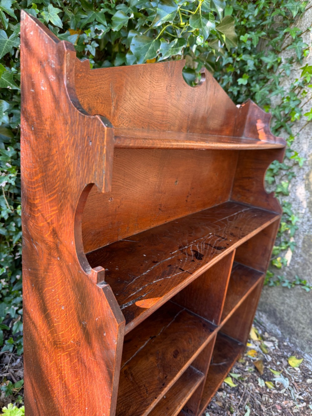 A small antique oak open bookcase featuring multiple shelf compartments, lower cubbies, and shaped side uprights. View XIII