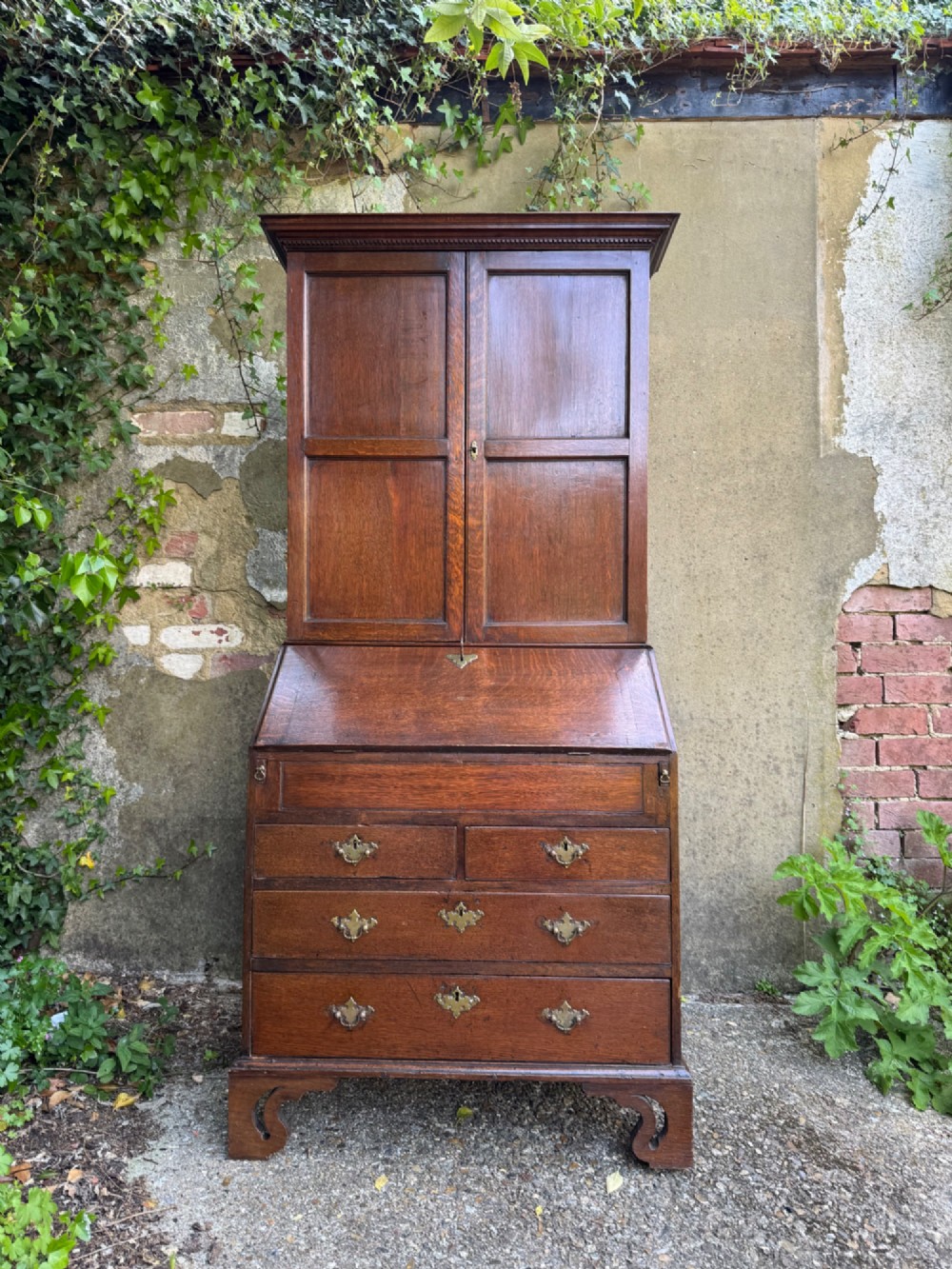 An antique warm brown oak bureau bookcase featuring twin fielded panel upper doors, a slant-front desk, and multiple drawers with brass hardware. View II