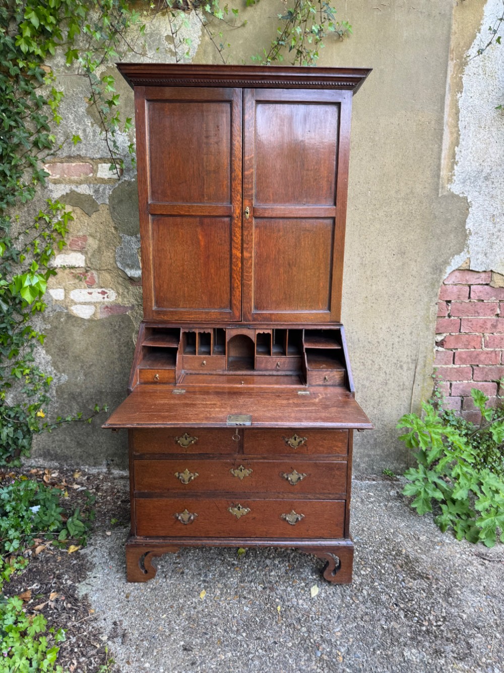 An antique warm brown oak bureau bookcase featuring twin fielded panel upper doors, a slant-front desk, and multiple drawers with brass hardware. View IV