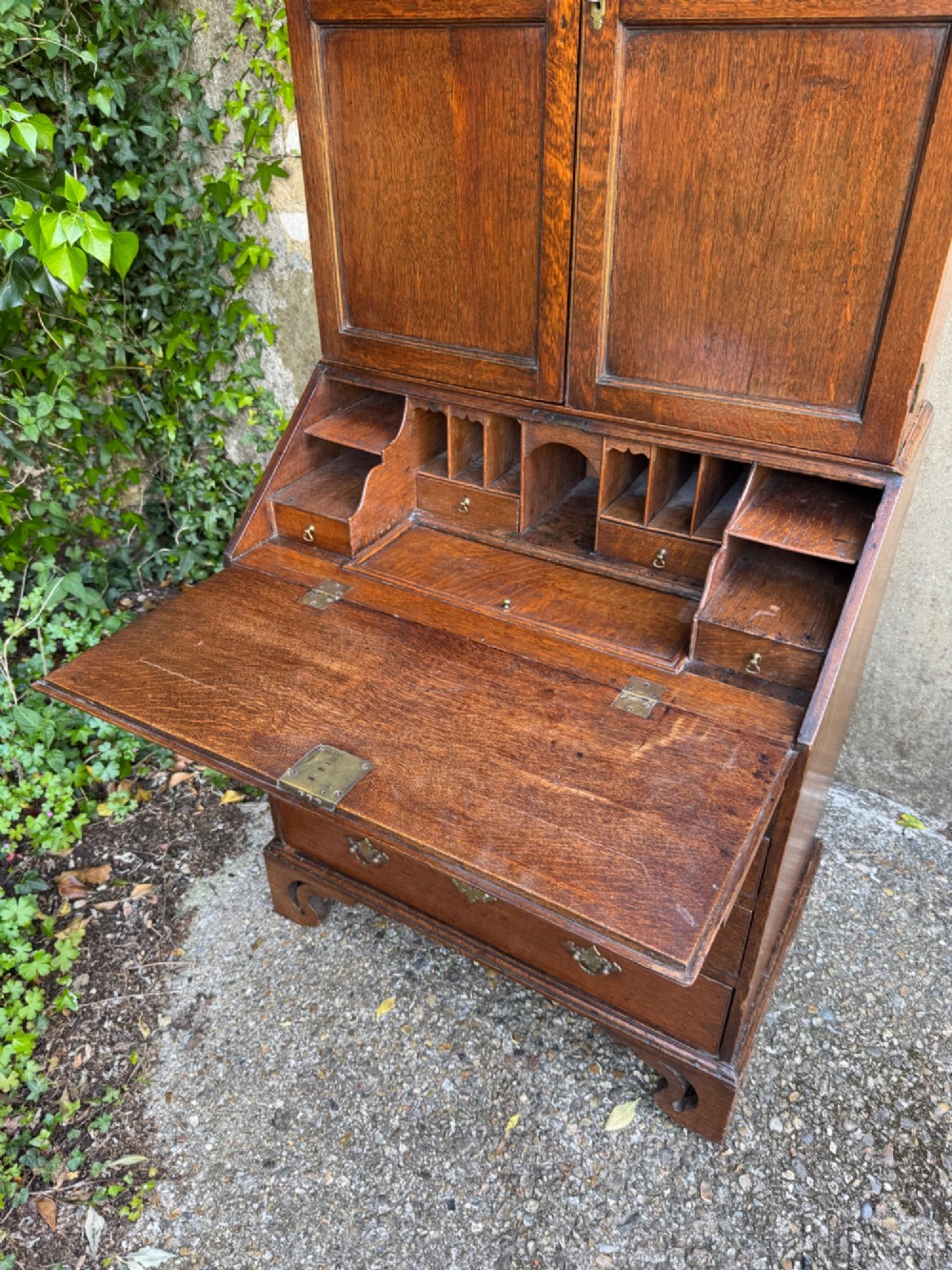 An antique warm brown oak bureau bookcase featuring twin fielded panel upper doors, a slant-front desk, and multiple drawers with brass hardware. View V