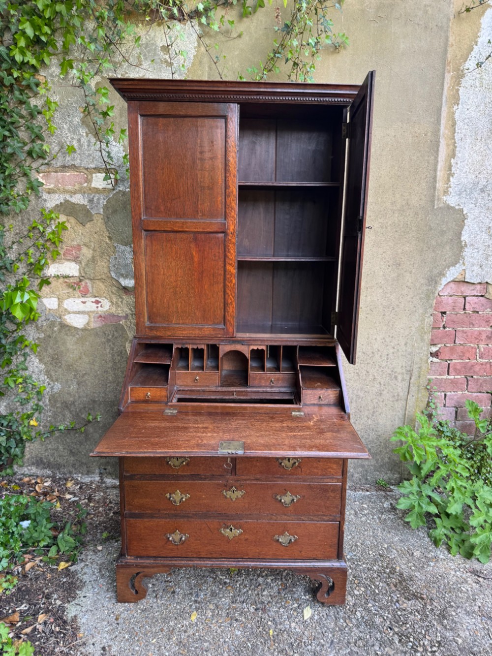 An antique warm brown oak bureau bookcase featuring twin fielded panel upper doors, a slant-front desk, and multiple drawers with brass hardware. View VI