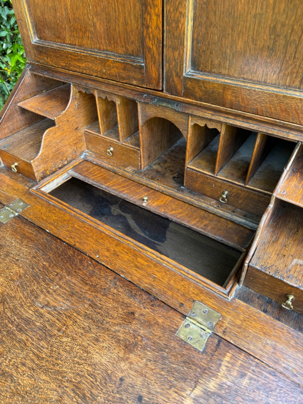 An antique warm brown oak bureau bookcase featuring twin fielded panel upper doors, a slant-front desk, and multiple drawers with brass hardware. View VII