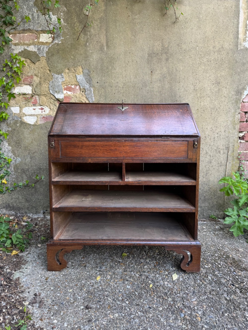 An antique warm brown oak bureau bookcase featuring twin fielded panel upper doors, a slant-front desk, and multiple drawers with brass hardware. View XV