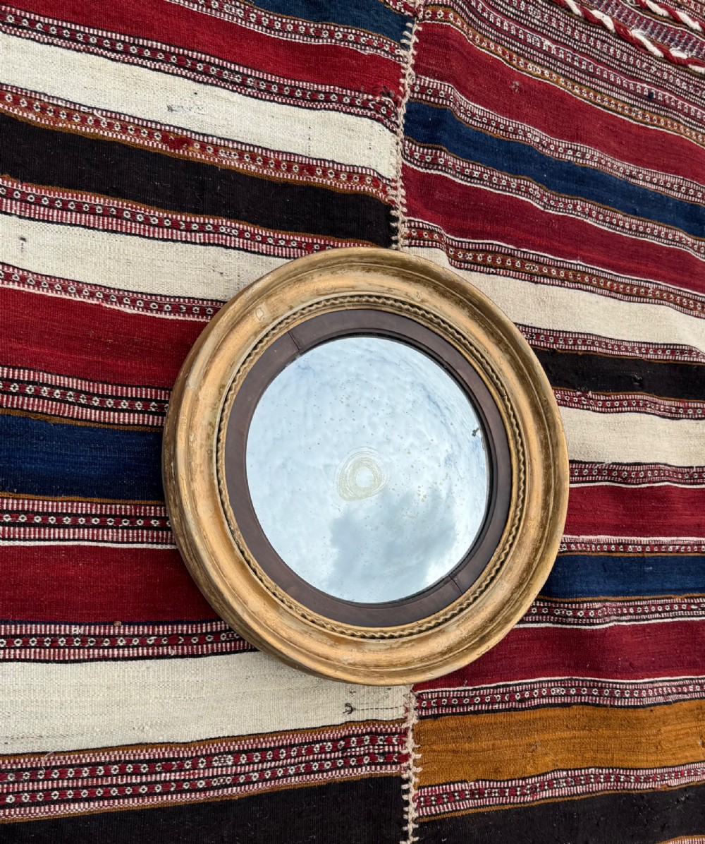A circular antique Regency convex mirror featuring a gilded moulded frame, an ebonised inner slip, and foxed glass.