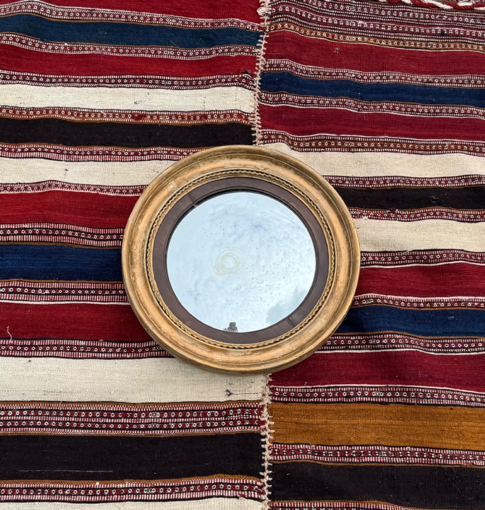 A circular antique Regency convex mirror featuring a gilded moulded frame, an ebonised inner slip, and foxed glass. View II