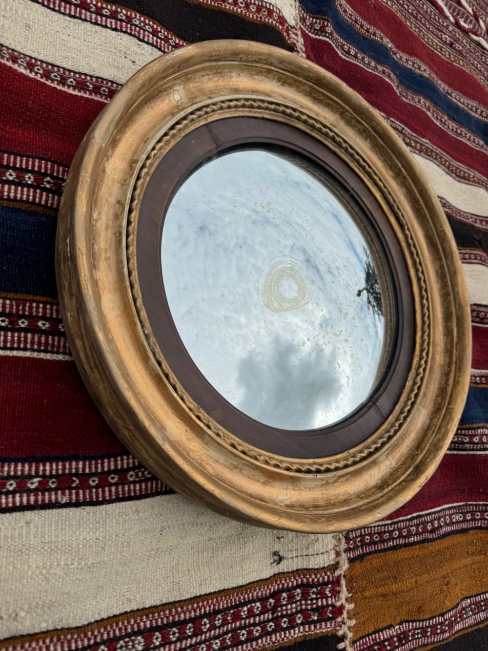 A circular antique Regency convex mirror featuring a gilded moulded frame, an ebonised inner slip, and foxed glass. View III