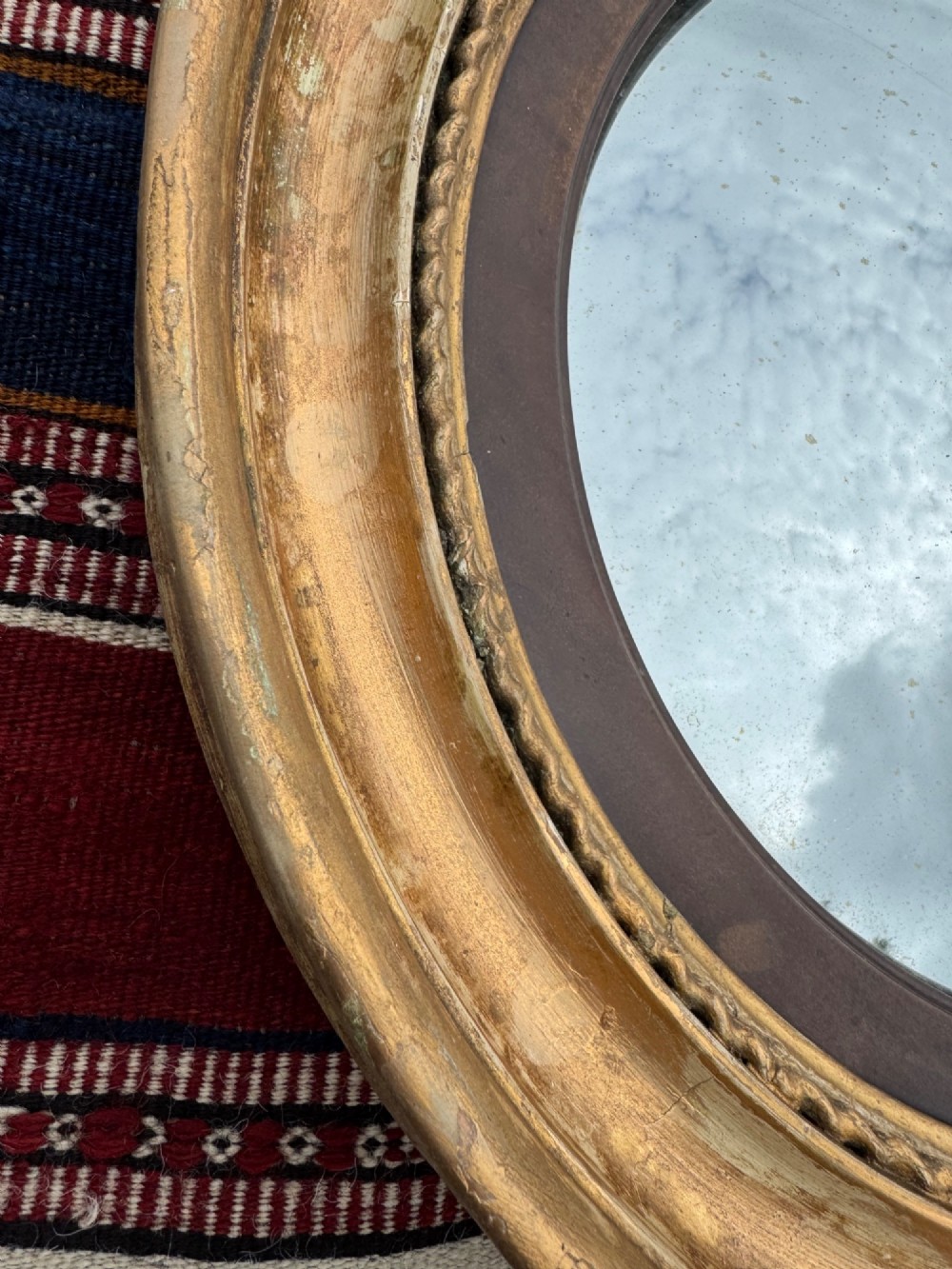 A circular antique Regency convex mirror featuring a gilded moulded frame, an ebonised inner slip, and foxed glass. View IV