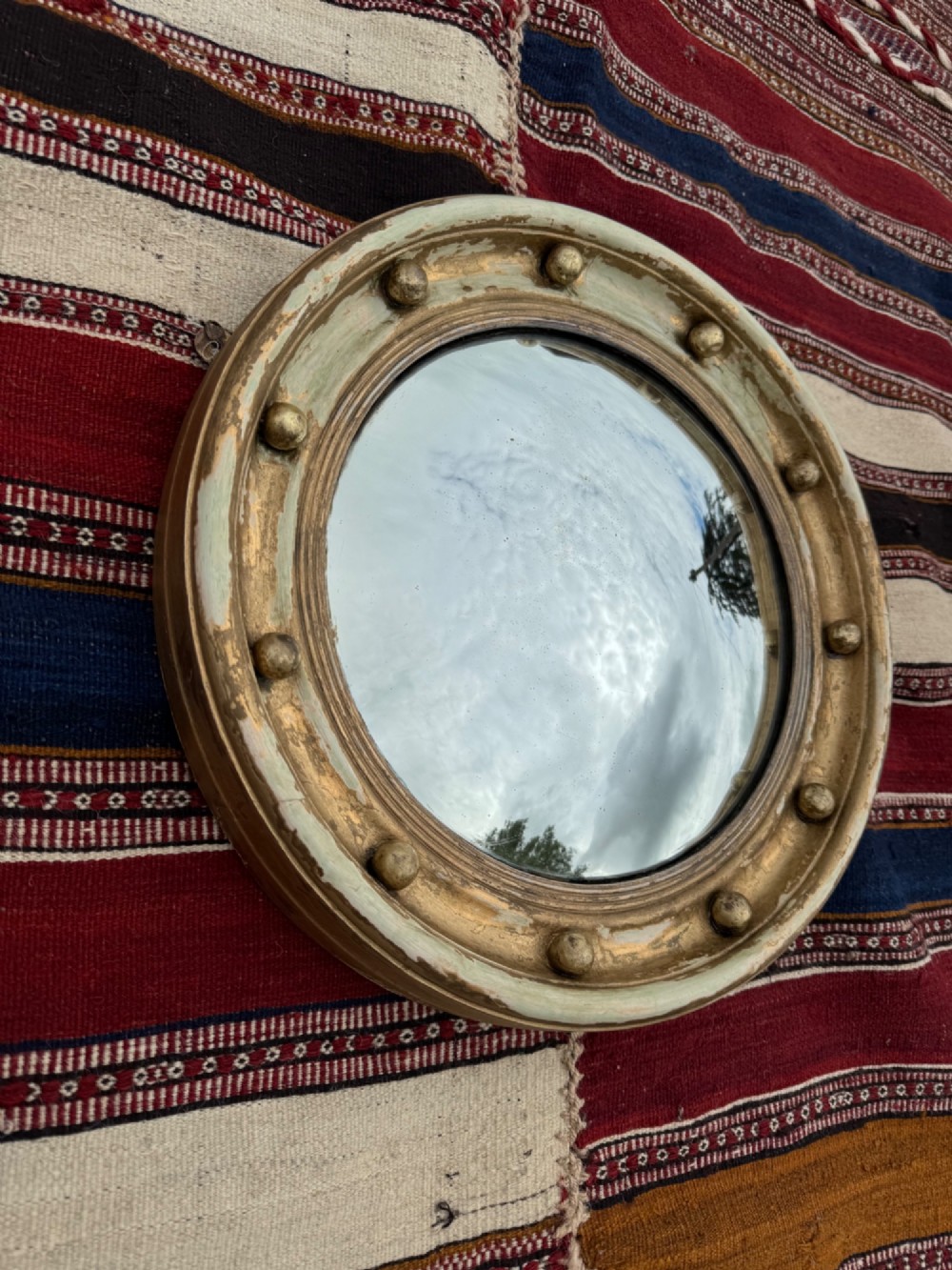 A circular antique convex mirror featuring a gilded and painted frame decorated with spherical balls along the inner rim. View II