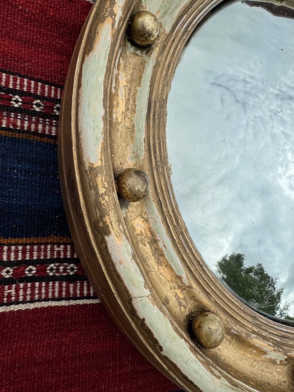 A circular antique convex mirror featuring a gilded and painted frame decorated with spherical balls along the inner rim. View IV