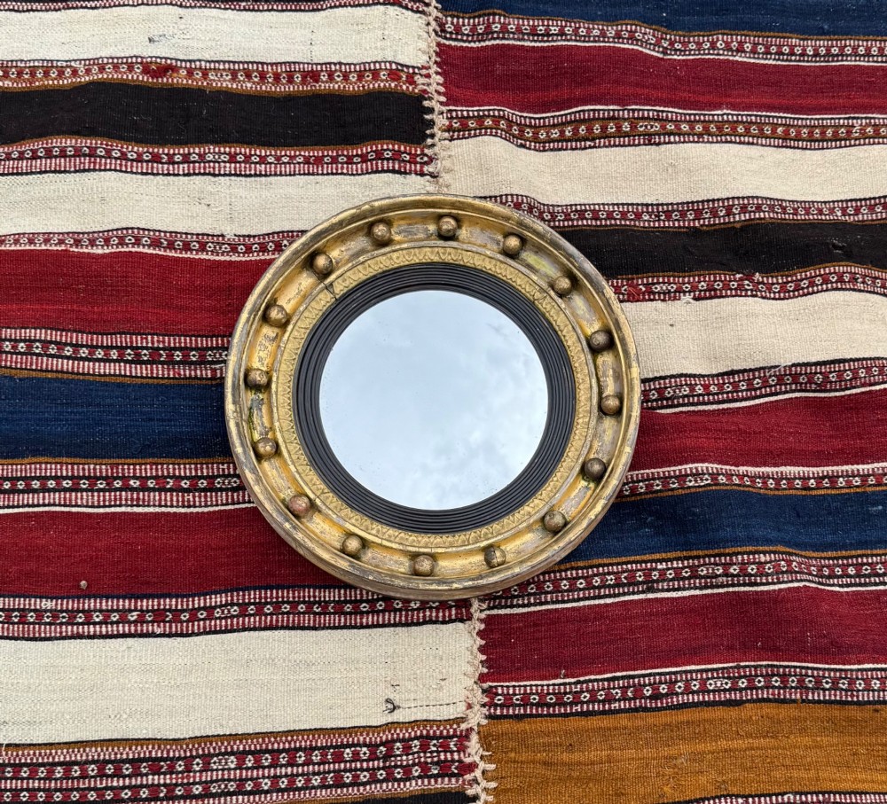 A circular antique giltwood convex mirror featuring a sphere-adorned outer frame and a dark reeded inner slip.