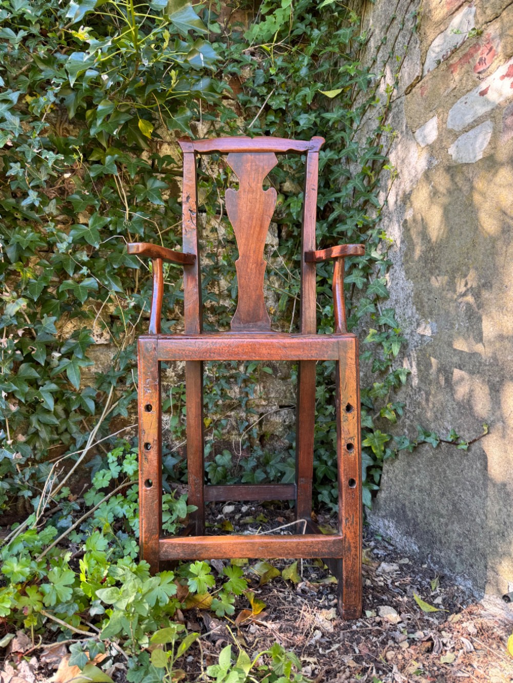 A dark brown Georgian wooden high chair with a central splat back, shaped armrests, square legs, and low wooden stretchers. View II
