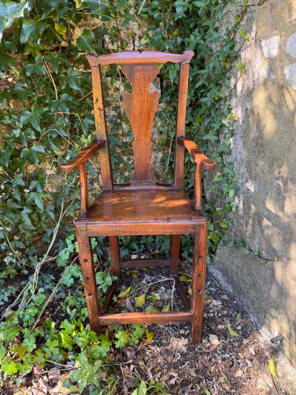 A dark brown Georgian wooden high chair with a central splat back, shaped armrests, square legs, and low wooden stretchers. View III