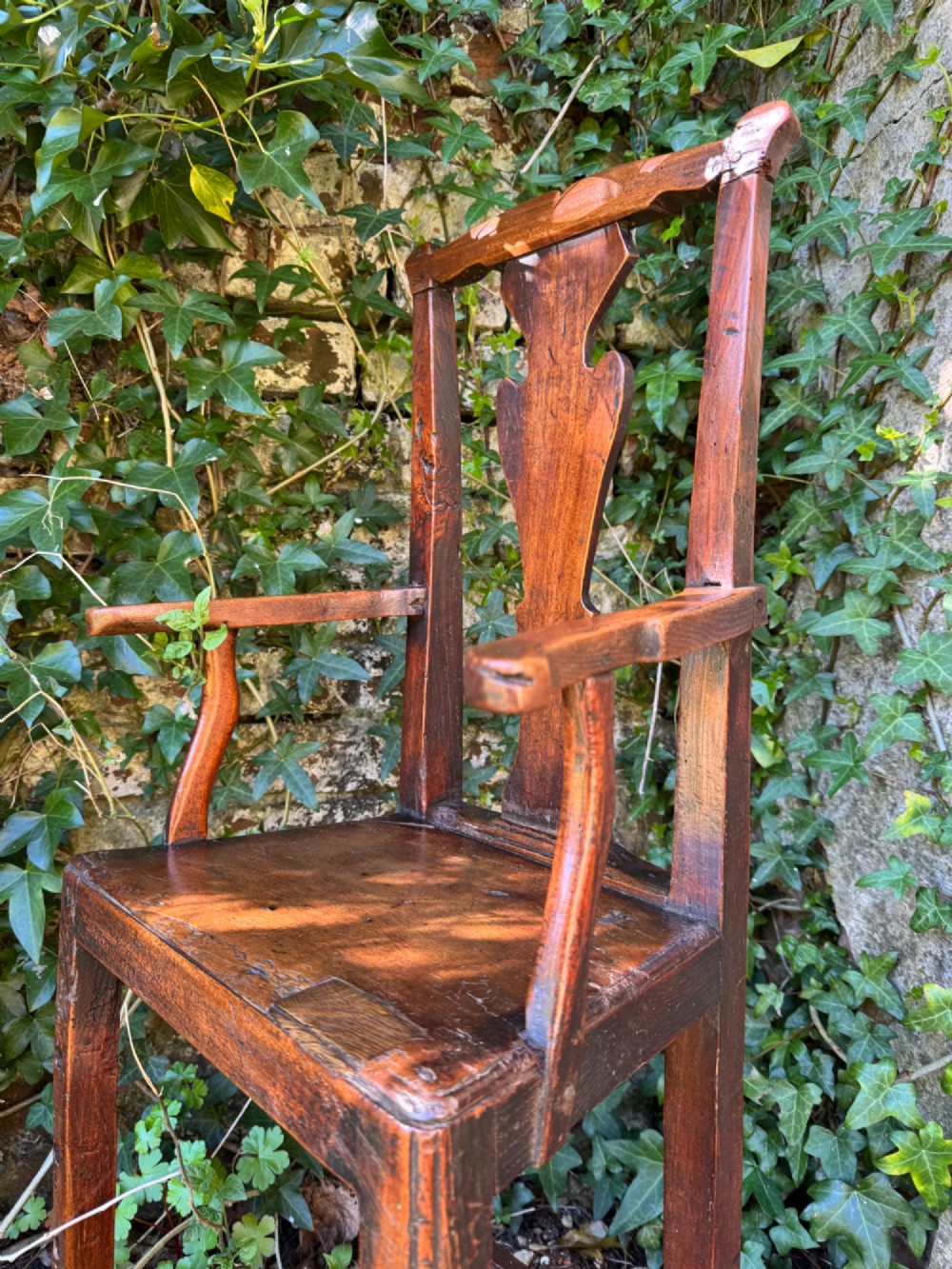 A dark brown Georgian wooden high chair with a central splat back, shaped armrests, square legs, and low wooden stretchers. View V