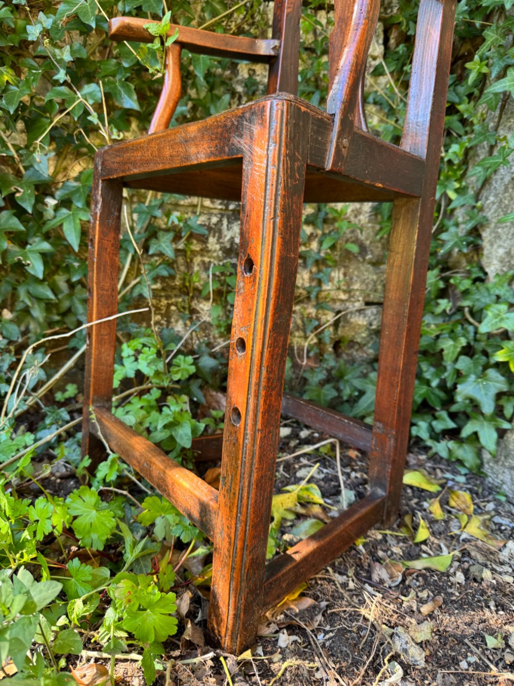 A dark brown Georgian wooden high chair with a central splat back, shaped armrests, square legs, and low wooden stretchers. View VI