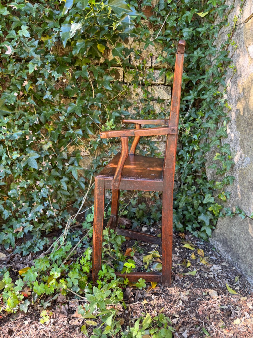A dark brown Georgian wooden high chair with a central splat back, shaped armrests, square legs, and low wooden stretchers. View VII