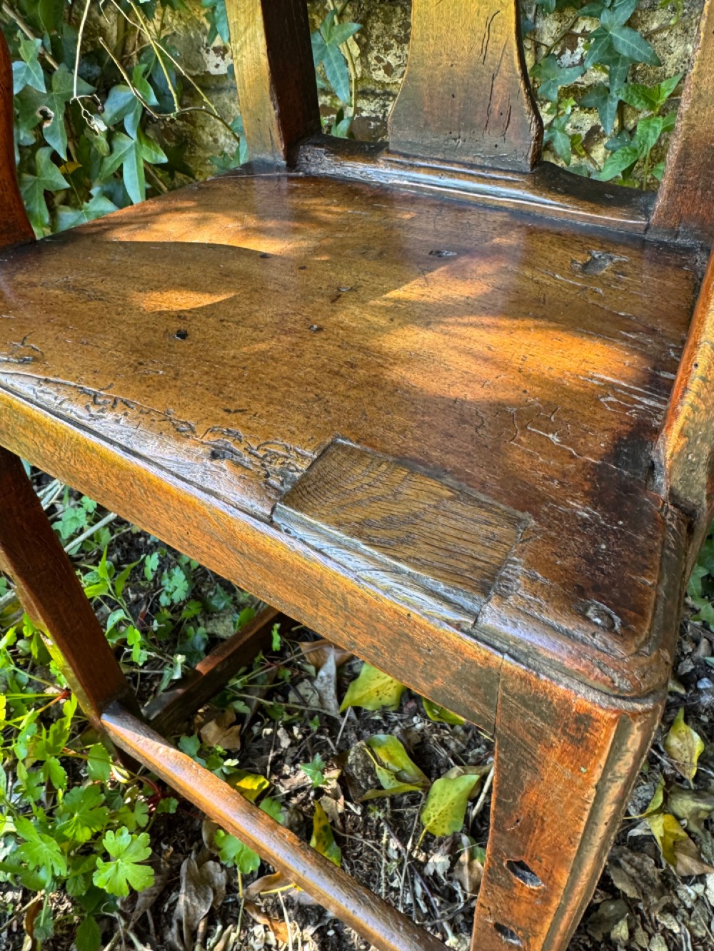 A dark brown Georgian wooden high chair with a central splat back, shaped armrests, square legs, and low wooden stretchers. View XIII