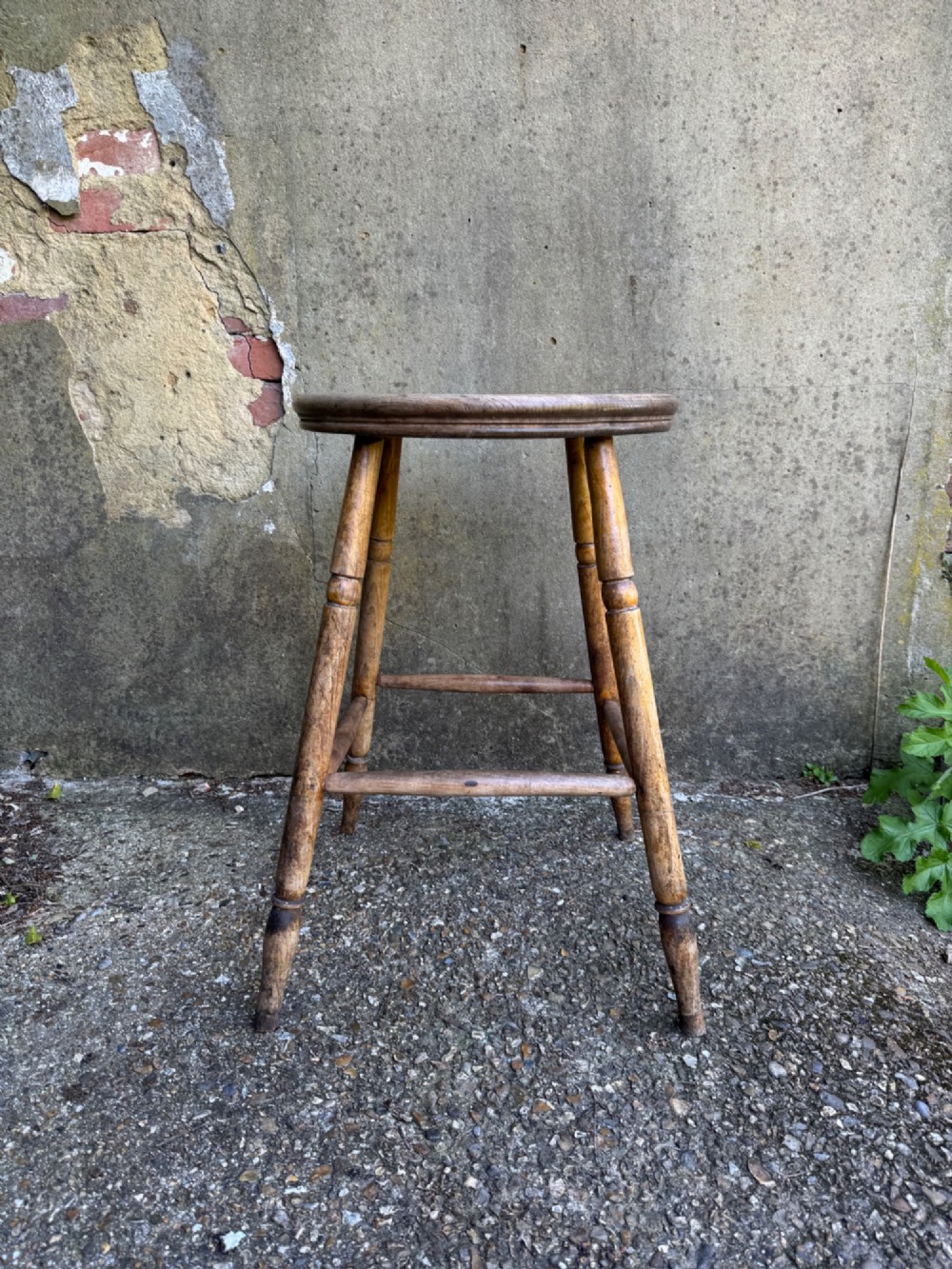 A rustic circular wooden stool featuring four splayed turned legs supported by horizontal timber stretchers. View II