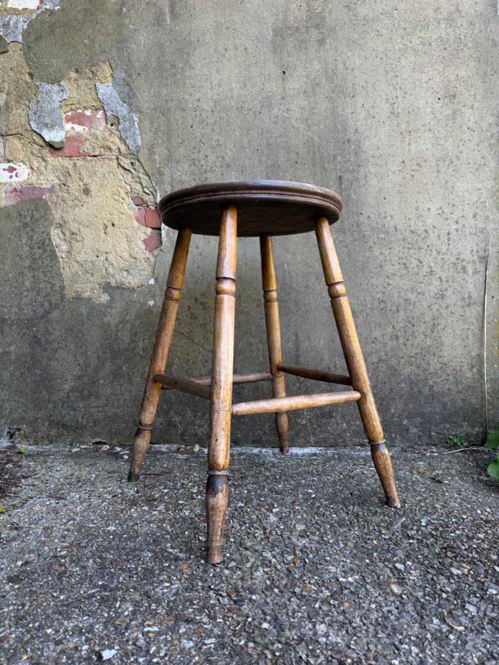 A rustic circular wooden stool featuring four splayed turned legs supported by horizontal timber stretchers. View IV
