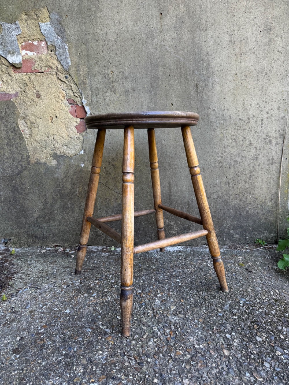 A rustic circular wooden stool featuring four splayed turned legs supported by horizontal timber stretchers. View V