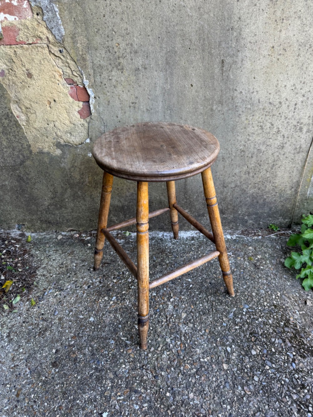 A rustic circular wooden stool featuring four splayed turned legs supported by horizontal timber stretchers. View VI