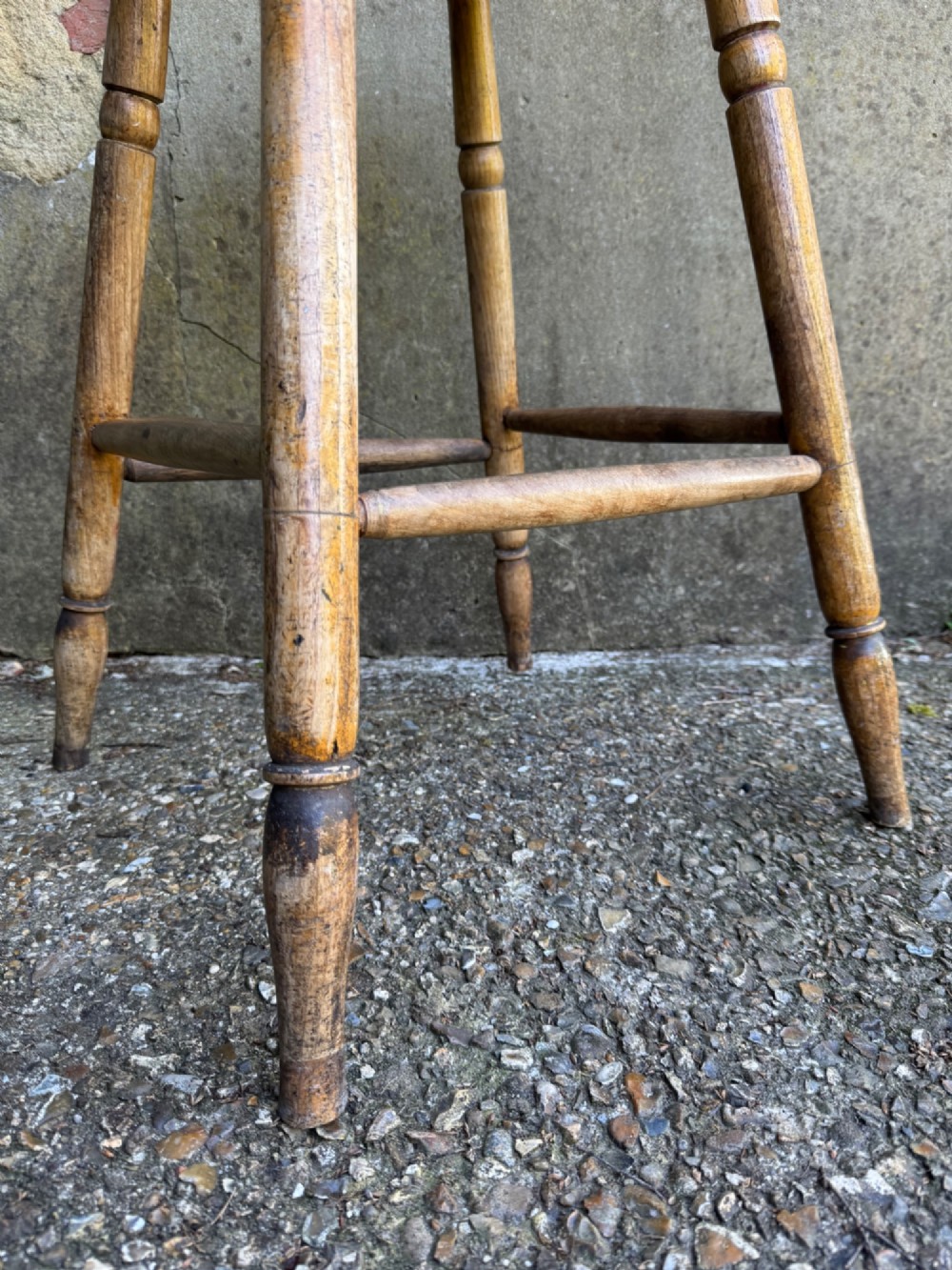 A rustic circular wooden stool featuring four splayed turned legs supported by horizontal timber stretchers. View VII