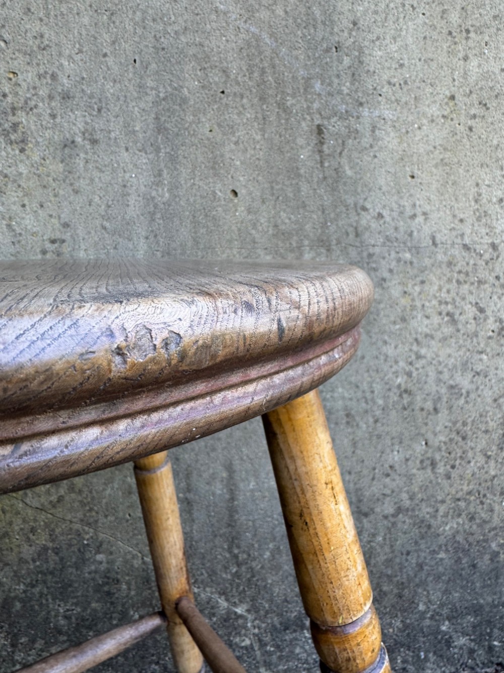 A rustic circular wooden stool featuring four splayed turned legs supported by horizontal timber stretchers. View IX