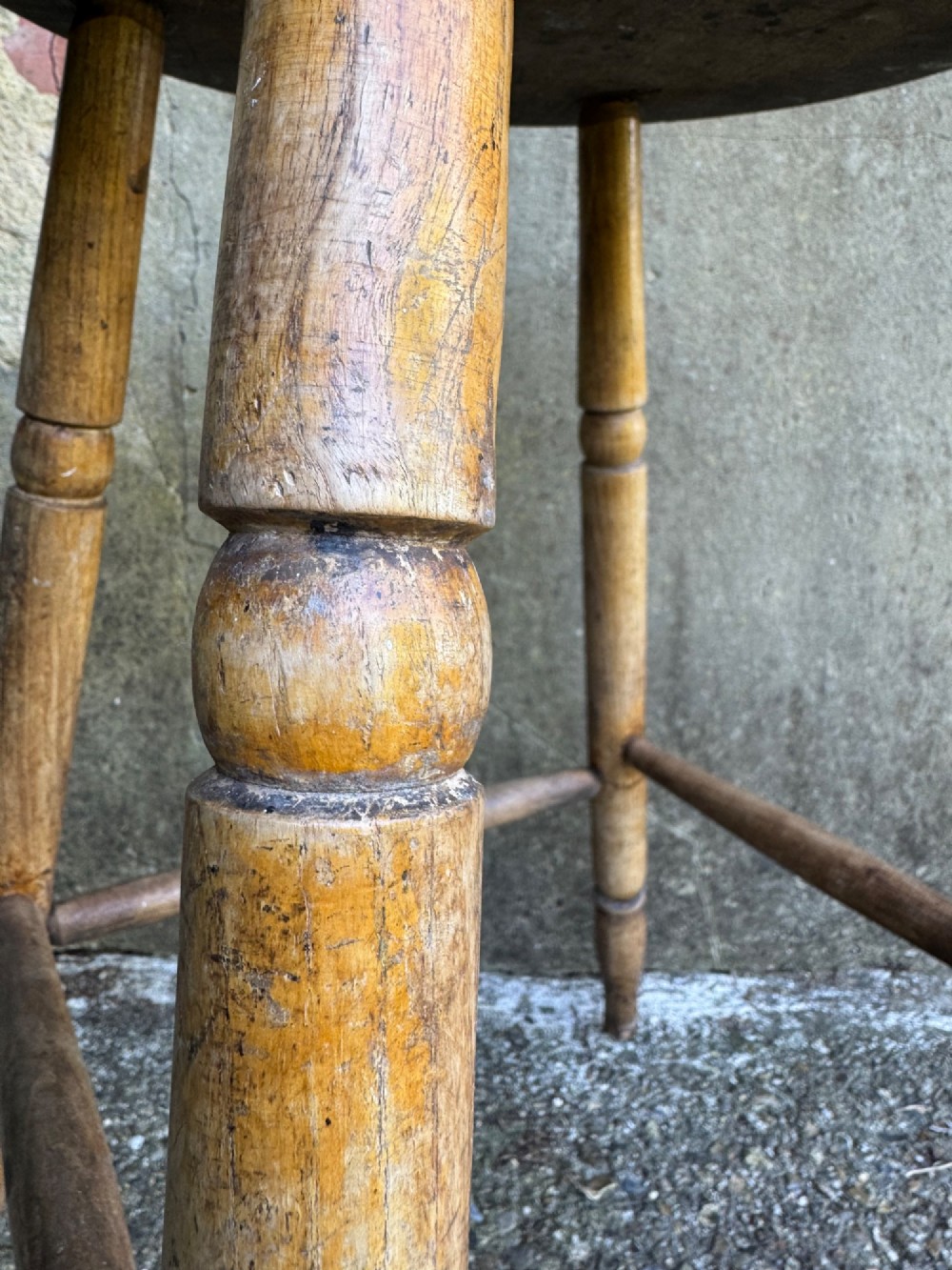A rustic circular wooden stool featuring four splayed turned legs supported by horizontal timber stretchers. View XI