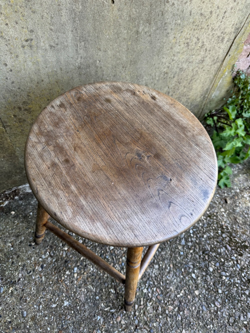 A rustic circular wooden stool featuring four splayed turned legs supported by horizontal timber stretchers. View XIII