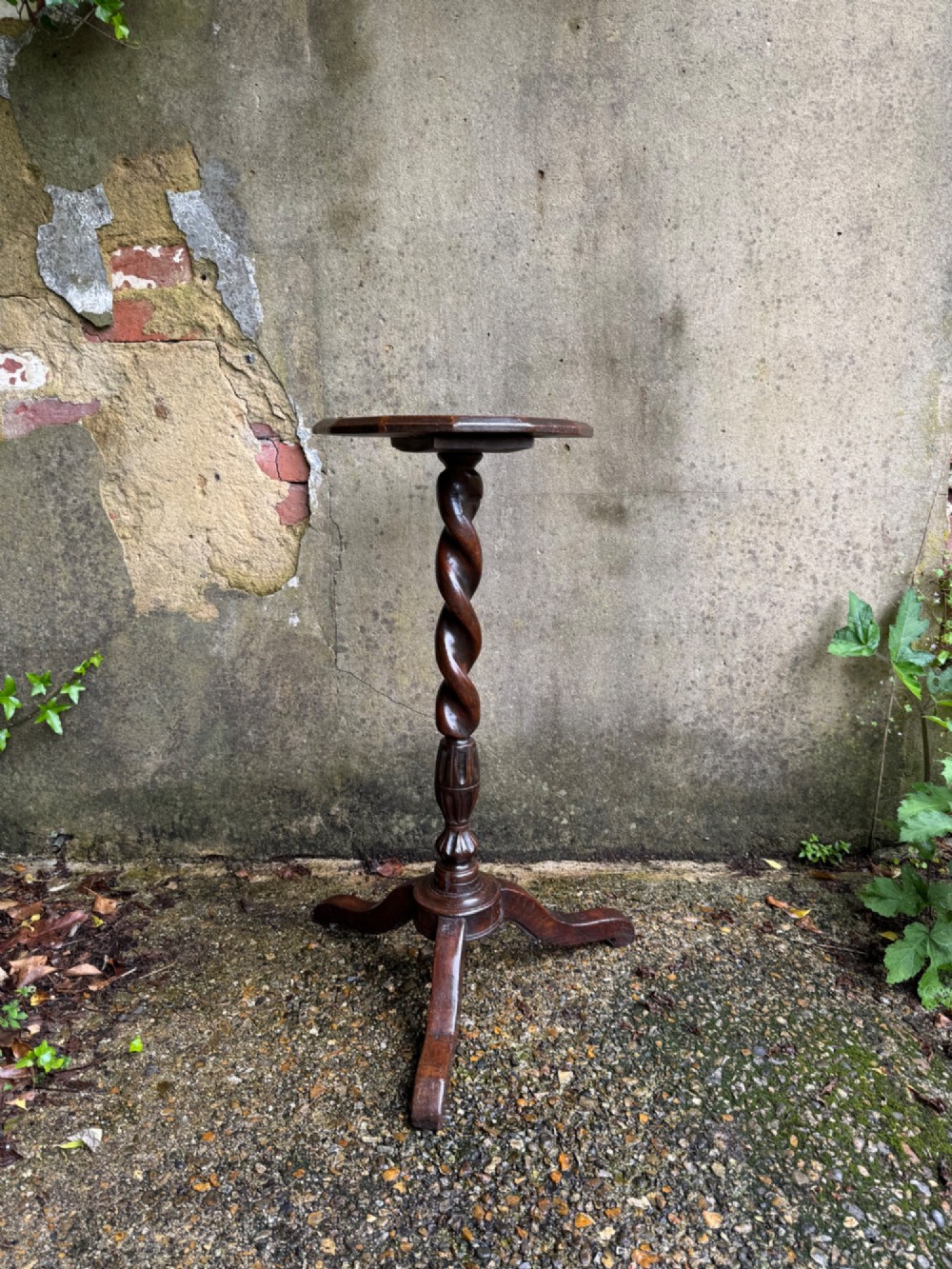 A tall dark oak side table featuring a circular top, a single barley twist column, and three splayed tripod legs.