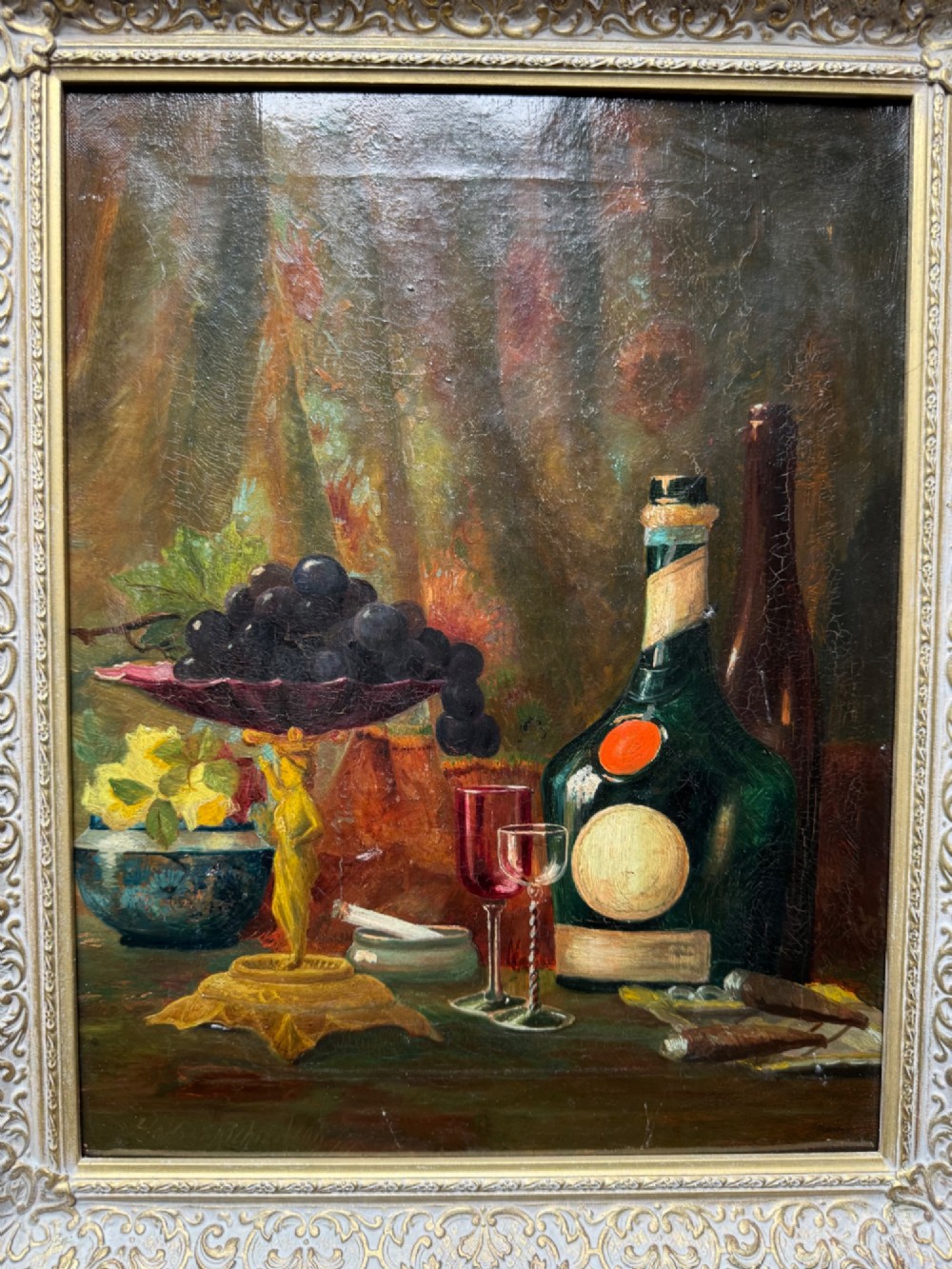 Antique framed oil painting depicting a still life composition with fruit, glassware, and bottles set in an ornate swept frame. View II