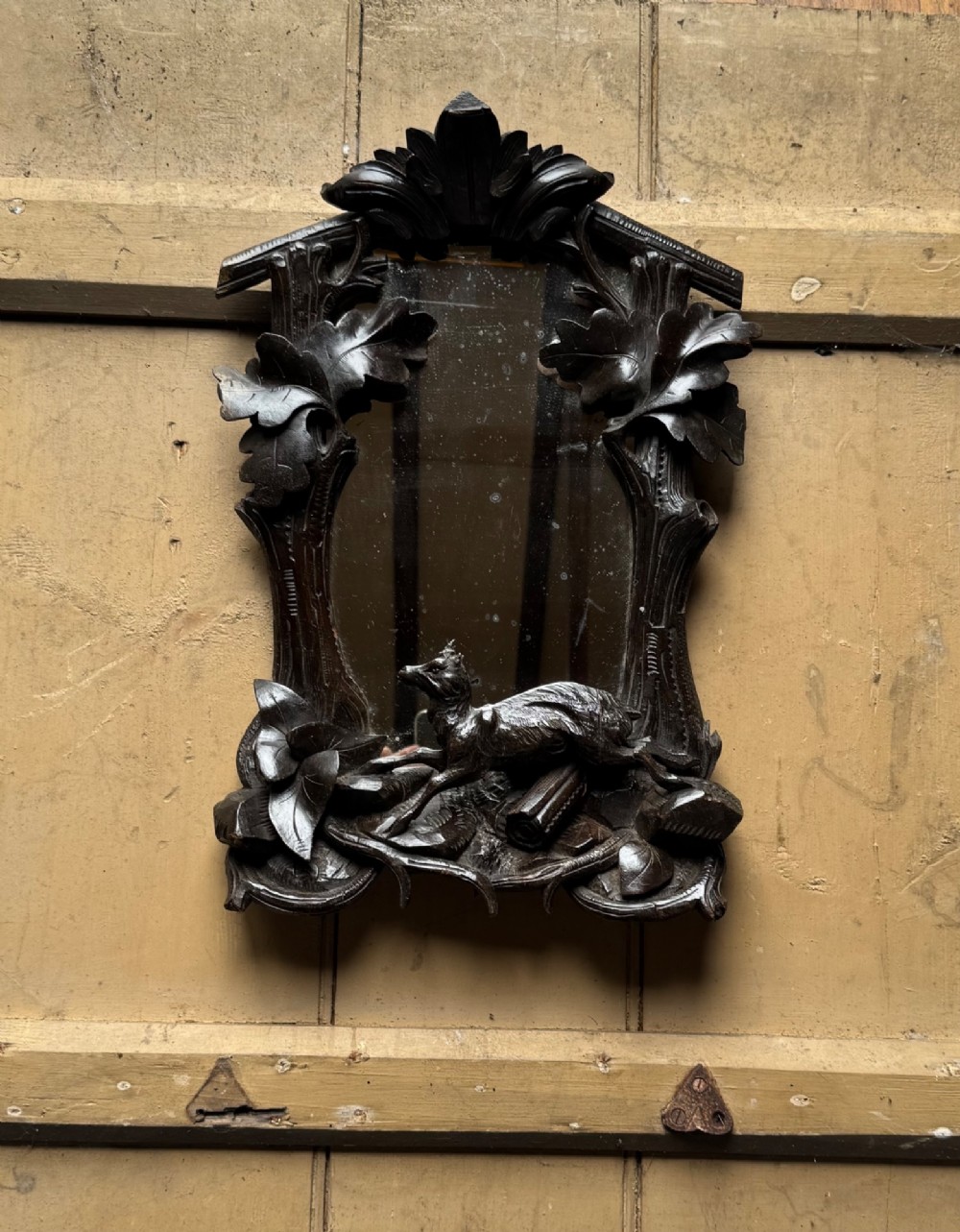 A dark hand-carved wooden wall mirror featuring a fox sculpted at the base surrounded by carved oak leaves and branches.