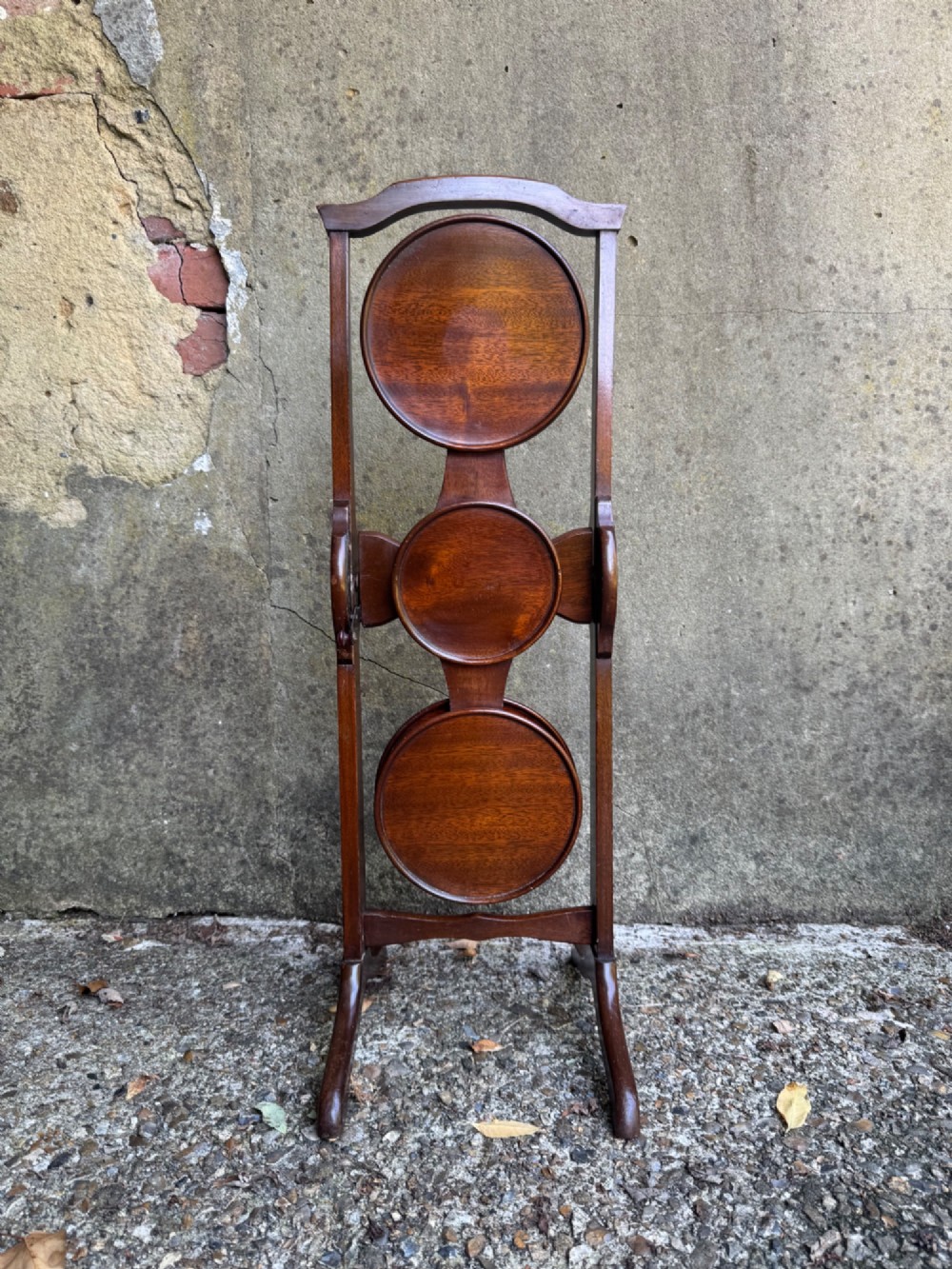 An antique mahogany monoplane folding cake stand with five circular wooden trays supported on a vertical frame with arched feet. View II