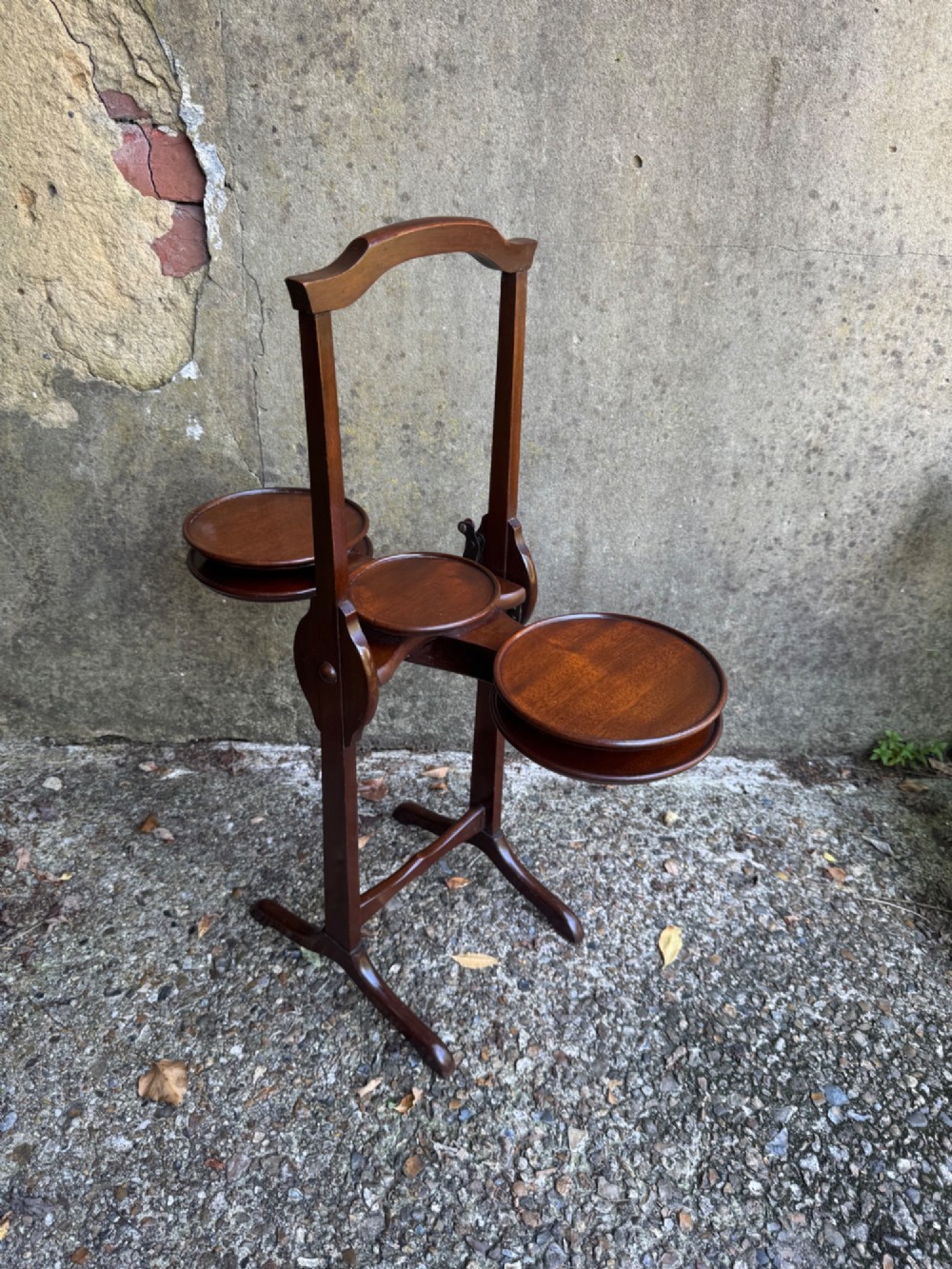 An antique mahogany monoplane folding cake stand with five circular wooden trays supported on a vertical frame with arched feet. View VI