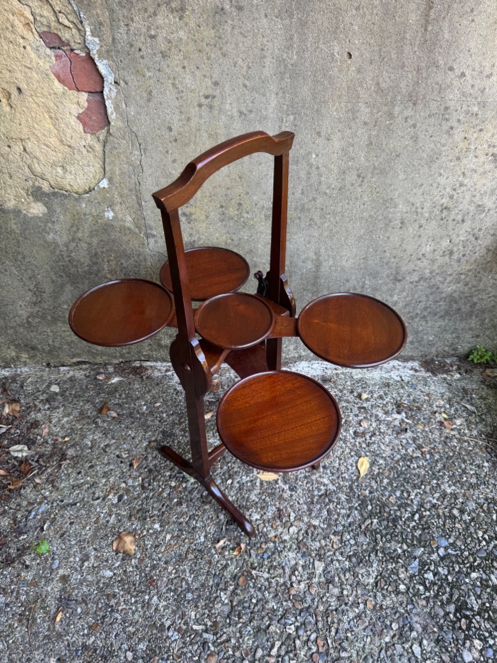 An antique mahogany monoplane folding cake stand with five circular wooden trays supported on a vertical frame with arched feet. View VII