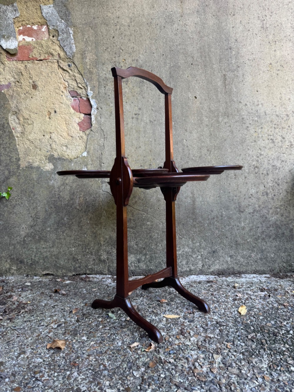 An antique mahogany monoplane folding cake stand with five circular wooden trays supported on a vertical frame with arched feet. View VIII