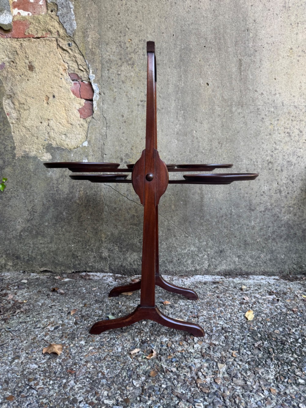 An antique mahogany monoplane folding cake stand with five circular wooden trays supported on a vertical frame with arched feet. View X